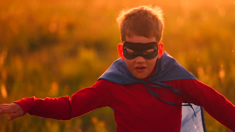 Junge-Im-Superheldenkostüm-Und-Mit-Maske-Rennt-Bei-Sonnenuntergang-Träumend-Und-Phantasievoll-über-Das-Feld.